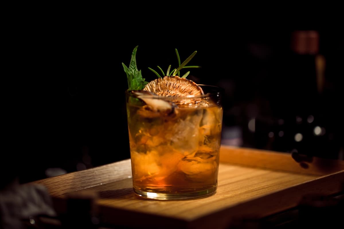 A dark cocktail garnished with rosemary on the bar