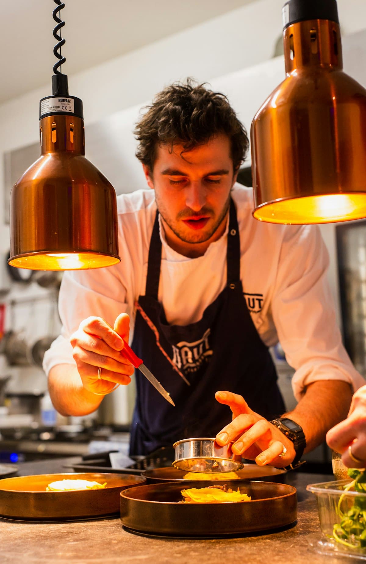 A chef plating a dish under warm copper lamps