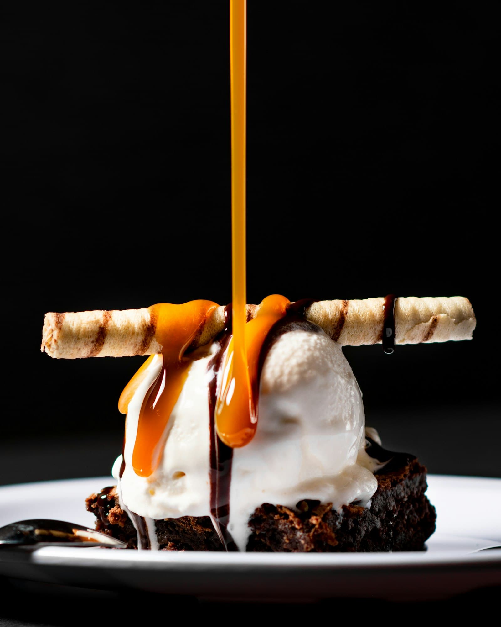 Caramel being poured over a plated dessert against black