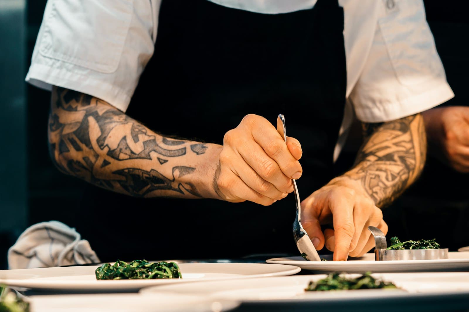 A chef's hands finishing two plates with herbs