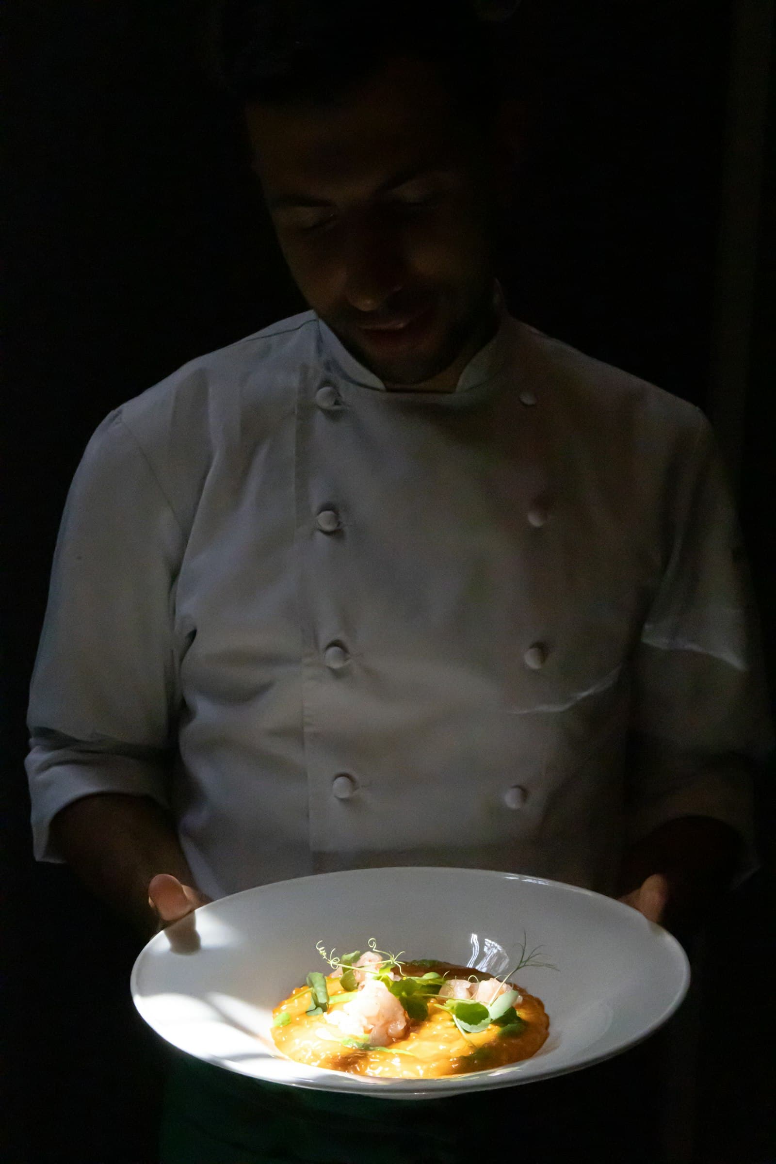 Chef Inés in her whites, standing in the half-light of the kitchen